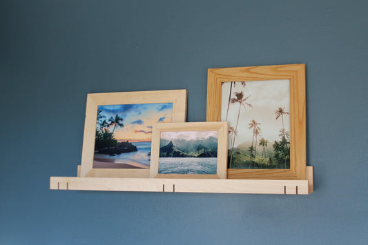 Maple 3-inch ledge shelf holding three framed tropical beach prints on a blue wall