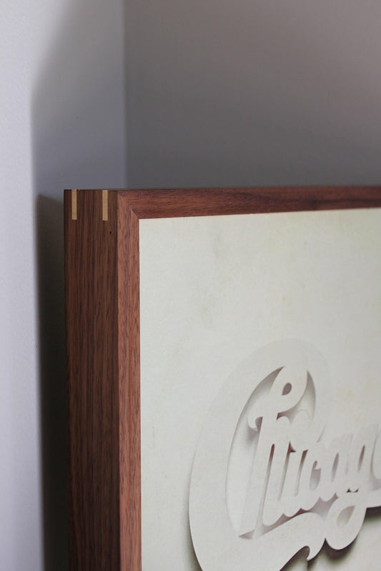 Close-up of a walnut album frame corner with maple spline and a white Chicago sleeve