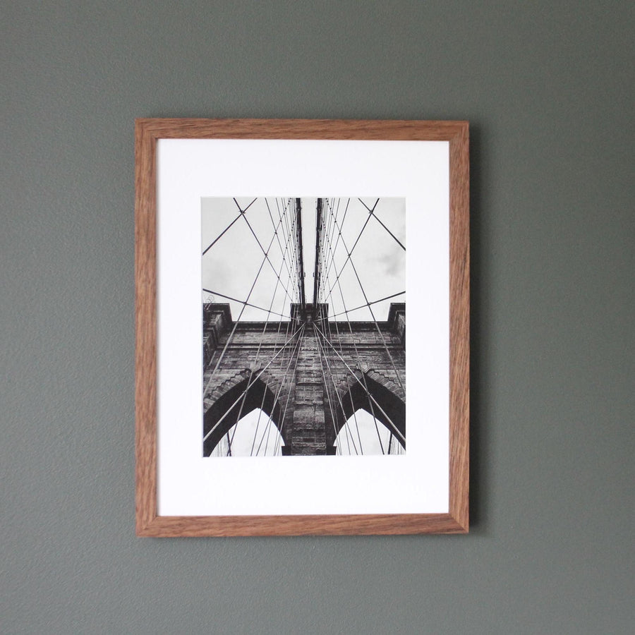 Black-and-white photo of the Brooklyn Bridge in a matted hardwood frame on a gray wall