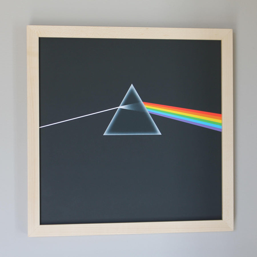 Album cover with a prism and rainbow design in a maple record frame on a gray wall