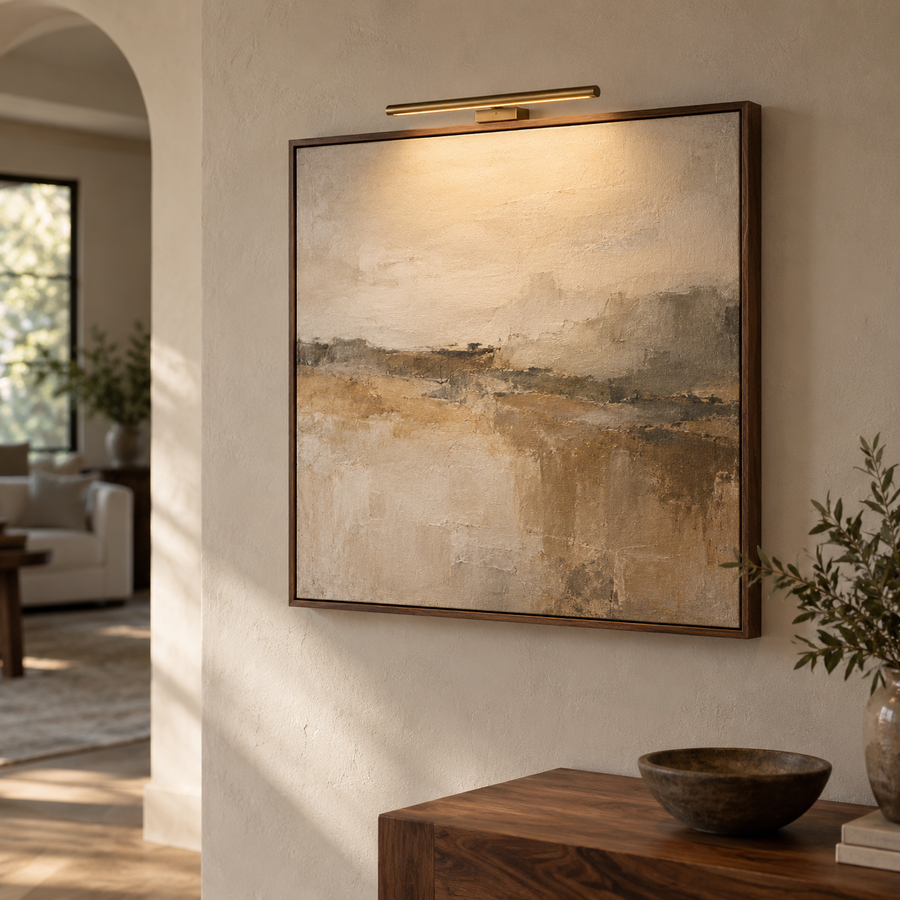 Walnut framed canvas illuminated by a wireless brass picture light on a warm plaster wall.