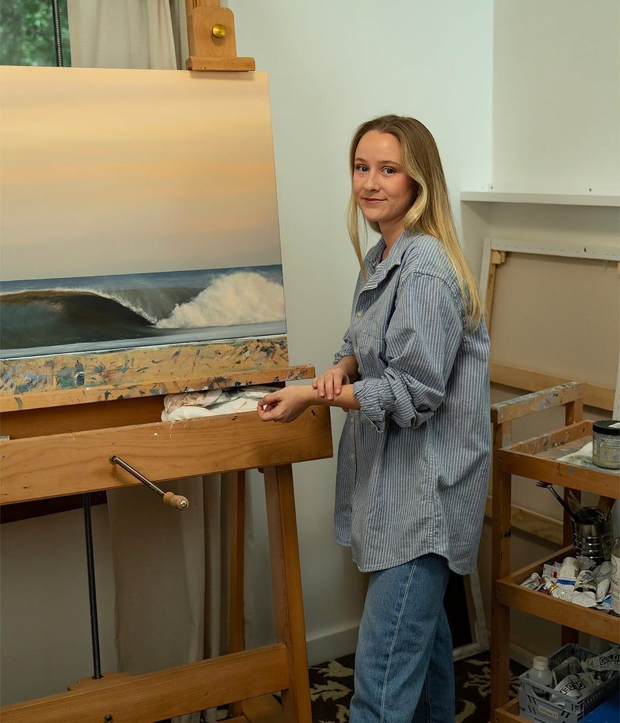 Painter Taylor Williams in her studio beside an easel with an ocean wave painting