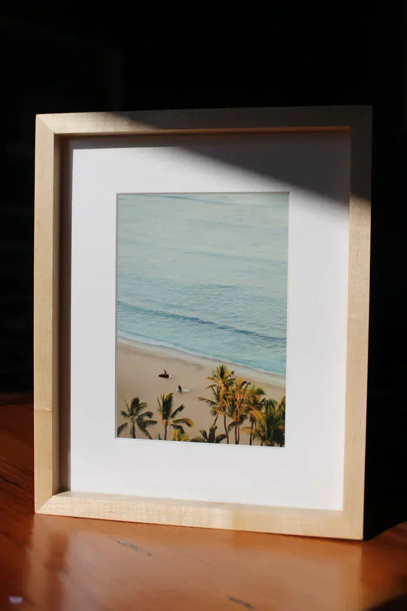 Matted beach photo in a maple frame catching sunlight on a wood table