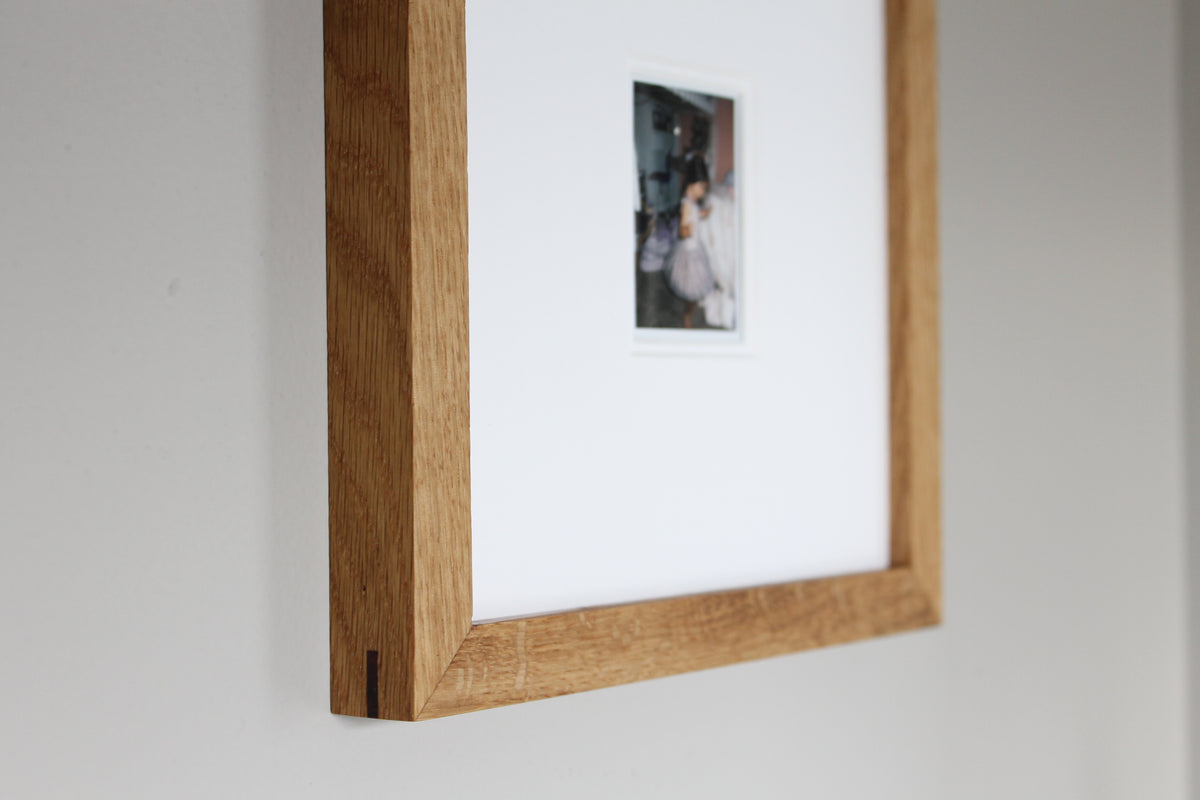 A small Instax print of my daughter, matted in a white oak frame on a gray wall