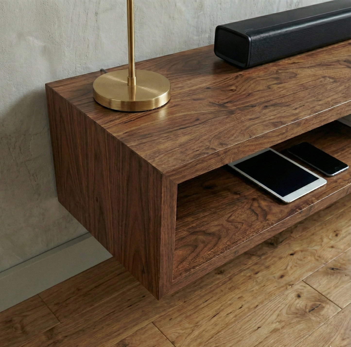 Wooden console table with electronic devices and a gold lamp on a wooden floor.