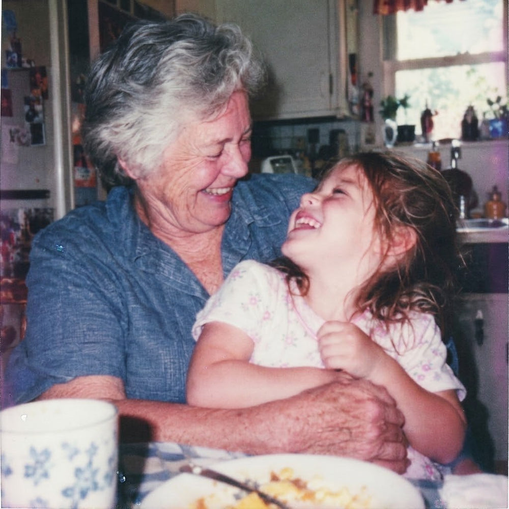 A grandmother and a little girl laughing together at the kitchen table, on an instant print